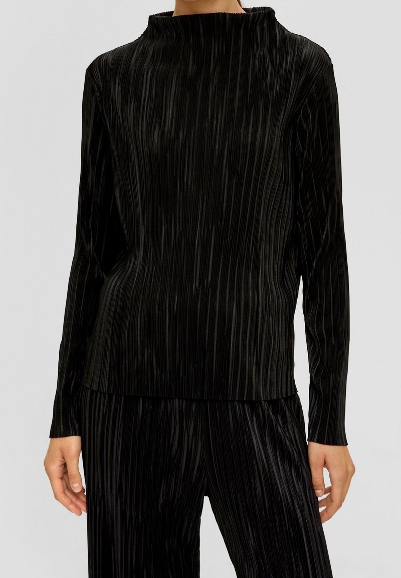 Haut noir plissé à manches longues et pantalon plissé assorti, avec un col rond haut et une coupe décontractée sur fond neutre.