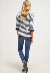 Mujer caminando away llevando una camiseta de rayas de manga larga, jeans azules con los puños doblados y zapatillas negras con cordones blancos.