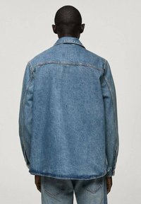 Chaqueta de mezclilla en azul claro, con un corte clásico, cuello puntiagudo, costuras laterales y detalles de costura a lo largo de los hombros y la espalda.
