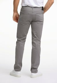 Grijze katoenen broek met een slim fit, voorzien van twee achterzakken, gestikte details, en gedragen met witte sneakers.