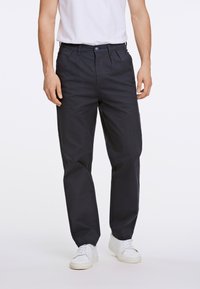 Pantaloni in cotone blu navy con design a gamba dritta, pieghe frontali e chiusura con bottone, abbinati a sneakers bianche.