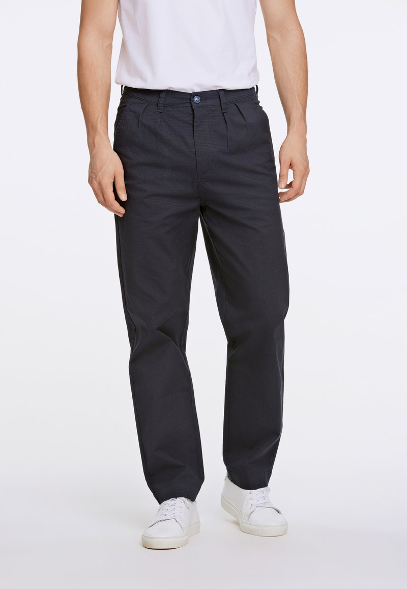 Pantaloni in cotone blu navy con design a gamba dritta, pieghe frontali e chiusura con bottone, abbinati a sneakers bianche.