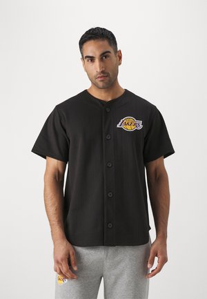 Camisa negra de botones con mangas cortas, que presenta rayas verticales y un colorido logo de Los Angeles Lakers en el lado izquierdo del pecho.