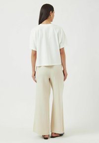 Hvit oversized kortermet topp paret med beige vide bukser. Stoffet virker lettvekts med en jevn tekstur. Svarte sandaler brukt.