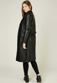 Manteau en cuir noir avec un design à double boutonnage, manches longues et taille ceinturée. Texture lisse, longueur genoux, poches latérales.