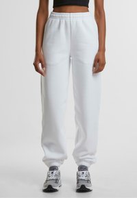 Witte trainingsbroek met een elastische tailleband en boorden, voorzien van een gladde textuur. Gekozen in combinatie met grijze en witte sport sneakers.
