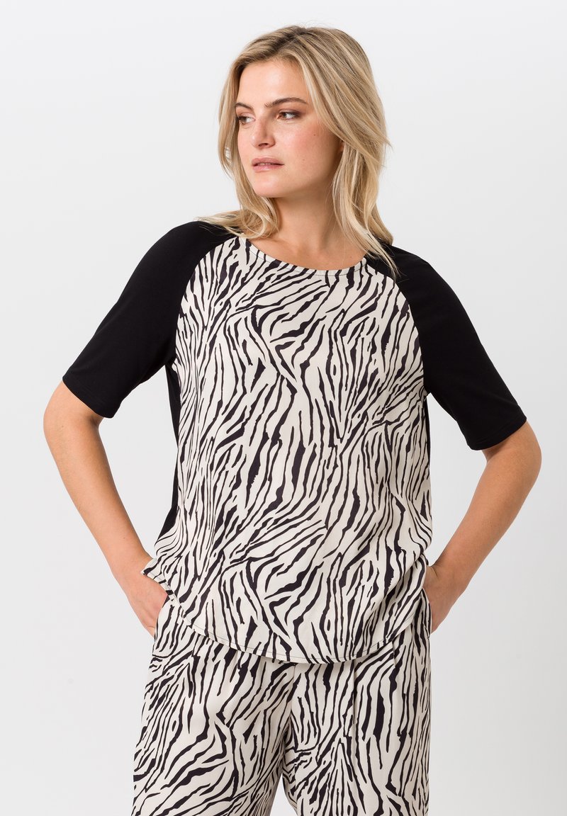 Korte mouwen top met een zwarte voorkant en een body met een zebra-patroon in roomkleur en zwart. Beschikt over een ronde halslijn en een ontspannen pasvorm.