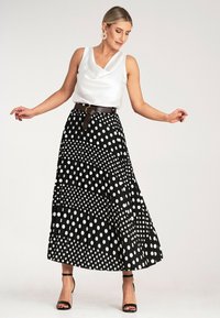 Czarna i biała spódnica w kropki z fałdami, połączona z białą satynową górą i brązowym paskiem. Otwarty przód czarnych szpilek dopełnia całość.