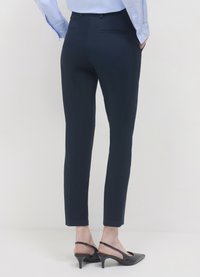 Pantalon ajusté bleu marine en tissu lisse, avec deux poches arrière et une silhouette élégante, associé à des escarpins noirs à bride arrière.