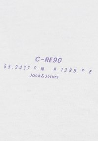 Baltos medvilnės audinys su violetiniais užrašais, kuriuose pateikti „C-RE90“ ir geografinės koordinatės. Įtraukta prekės ženklo „Jack&Jones“ pavadinimas.