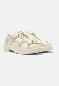 Scarpe di pelle color crema con punta tonda, caratterizzate da unici dettagli a fiocco e lacci piatti, montate su una suola spessa.