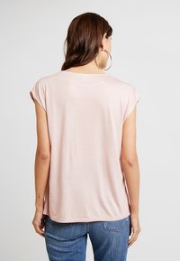Light pink short-sleeve top, soft fabric, relaxed fit, slight sheen, rounded neckline, and no visible patterns or accents. Worn with denim jeans.