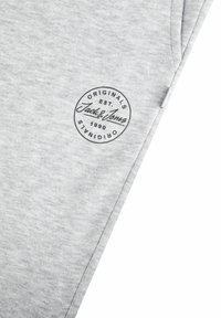 Graue Baumwoll-Sweatpants mit einem runden schwarzen Logo, das die Schriftzüge "Originals" und "Jack & Jones", gegründet 1990, zeigt. Weiches, strukturiertes Material.