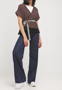 Topp med svart texturerat mönster, korta ärmar och spetsdetaljer. Kombineras med högmidjade marinblå vida byxor och vita sneakers.