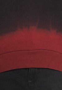 Gros plan sur une couture en tissu dégradé noir et rouge au-dessus d'un jean en denim noir.