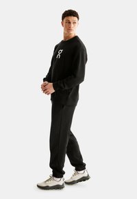 Black sweatshirt with logo, paired with black joggers and light gray athletic shoes. Smooth fabric, relaxed fit, and elastic cuffs.