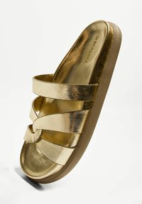 Gold metallic slide sandals with crossed straps. Smooth texture and rounded toe shape. Light brown sole, featuring brand name inside.