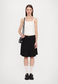 Bílý strukturovaný crop top s ramínky, v kombinaci s černou plisovanou sukní. Černá kabelka, bílé ponožky a robustní černé boty doplňují celý vzhled.