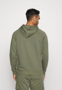 Olivegrüner Hoodie aus weichem Stoff, mit Kapuze und Raglanärmeln. Das Design umfasst einen gerippten Saum und Ärmelbündchen für eine enge Passform.