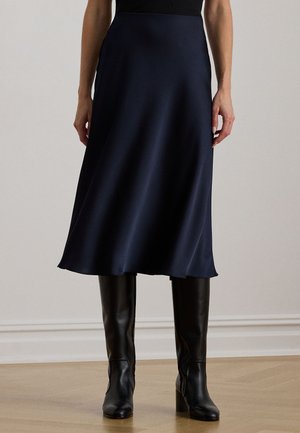 Μπλε σατέν μίντι φούστα με ρομαντική σιλουέτα, που διαθέτει απαλό υφή, ελαφρώς φαρδιά φάσα και φοριέται με μαύρες δερμάτινες μπότες μέχρι το γόνατο.