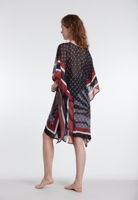 Prosojen črn kaftan z rdečimi, belimi in sivimi geometrijskimi črtami; lahkoten material z ohlapnim krojem in širokimi rokavi.
