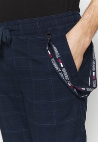Pantalones de cuadros azul marino con cintura elástica, que incluyen un cordón y un bolsillo lateral con una correa de marca Tommy Jeans.