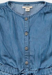 Vaate denim-kankaasta vaaleansinisessä sävyssä, jossa on pyöreä pääntie, viisi harmaan sävystä nappia edessä ja säädettävä nyöri vyötäröllä. Sileä pinta.