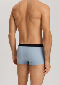 Ljusblå herrboxershorts med svart elastiskt midjeband, figurnära design, slät textur och minimal stil.