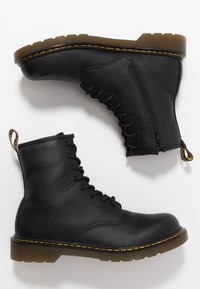 Botas de tobillo de cuero negro con frente de cordones, cremallera lateral y suela de goma texturizada. Cuenta con costuras amarillas y una lengüeta.