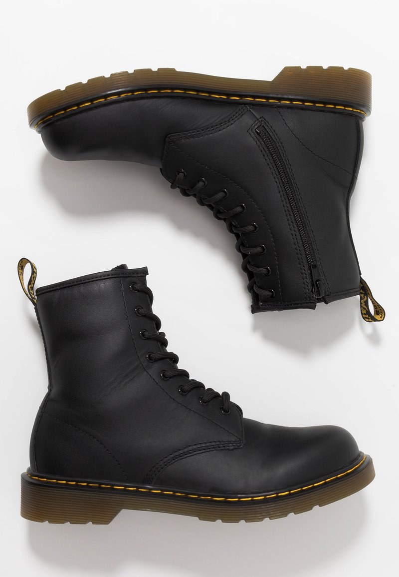 Botas de tobillo de cuero negro con frente de cordones, cremallera lateral y suela de goma texturizada. Cuenta con costuras amarillas y una lengüeta.
