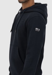 Marineblauwe hoodie met een voorvak, een trekkoordcapuchon en een logopatch op de linkermouw. Gemaakt van zachte, gestructureerde stof.