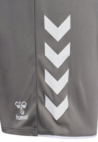 Grauer Stoff mit vier weißen, nach unten zeigenden Schrägstrichen und einem kleinen Logo mit einer stilisierten Biene und dem Schriftzug "hummel" nahe dem Saum.