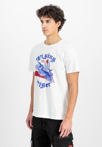 Hvid bomulds T-shirt med et blåt grafisk motiv af en vinger tiger og teksten "Flying Tiger". Korte ærmer, rund halsudskæring og regular fit.