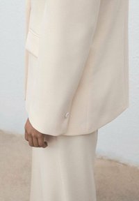 Lichtcrème, op maat gemaakte blazer met een enkele zilveren knop, met een geknipt revers en een gestructureerde schouder, in combinatie met bijpassende broek.