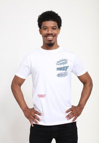 Hvid bomulds T-shirt med tegneserie-lignende grafik i blå og sort, med et rødt mærke der står "85 År med Superman" på nederste kant.