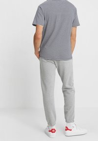 Pruhované tričko s kulatým výstřihem v námořnické modré a bílé barvě, spárované se šedými tepláky s elastickými manžetami a bílými teniskami s červenými akcenty.
