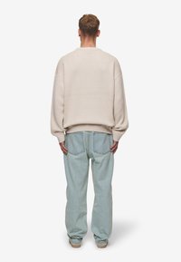 Beige, oversized stickad tröja med sänkt axelsöm, ribbstickade mudd och nederkant, parrad med ljusblå, avslappnade jeans med bakfickor.