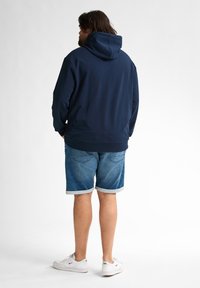 Hanorac cu glugă de culoare bleumarin, cu o croială lejeră, asortat cu pantaloni șort din denim deschis, cu margini răsucite și adidași albi. Material texturat.