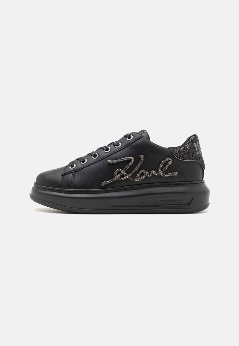 Sneaker en cuir noir avec un design à lacets plats, présentant un accent noir texturé au talon et un détail scintillant de signature le long du côté.