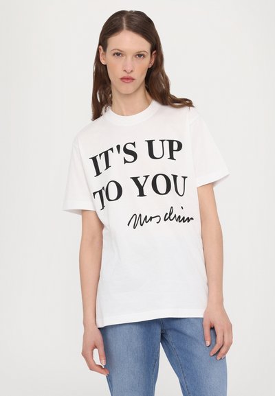Vit bomull t-shirt med korta ärmar. Svart text med orden "DET ÄR UPP TILL DIG" med en handskriven signatur nedanför. Enkel design, rundad halsringning.
