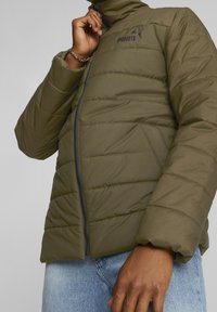 Doudoune vert olive avec un col haut, motif matelassé diagonal, fermeture éclair frontale et un petit logo noir sur la poitrine. Tissu texturé.