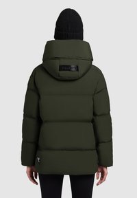 Opgeblazen olijfgroene jas met een grote capuchon, doorgestikt ontwerp, en een zwarte logopatch bij de nek. Heeft een geribbelde zwarte gebreide muts.