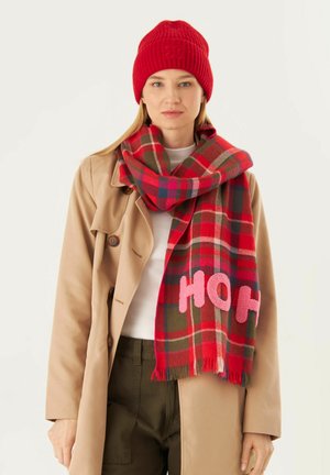 Bonnet rouge à côtes et écharpe à carreaux rouge, vert et bleu, avec des lettres "HOH" en rose. L'écharpe a des bords frangés et une texture douce.