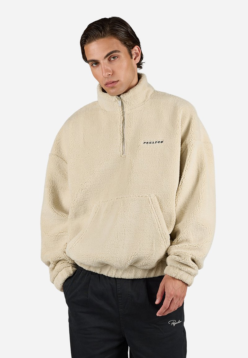 Beżowy polarowy sweter z półzamkiem, kangurzą kieszenią z przodu, ściągaczem przy hemie i mankietach oraz logo na klatce piersiowej. Miękka faktura.