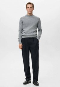 Maglione grigio in lana con scollo rotondo, abbinato a pantaloni blu scuro e scarpe in pelle nera, esposto su uno sfondo neutro.