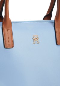 Ανοιχτό μπλε συνθετικό τσάντα χειρός με καφέ δερμάτινες λαβές και ασημένιο λογότυπο «TH», με κλείσιμο με φερμουάρ και υφή.