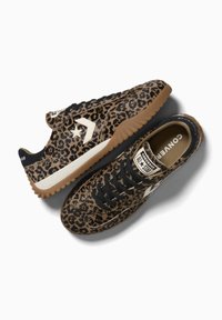 O pereche de adidași Converse All Star cu imprimeu leopard maro și negru, șireturi negre, logo stea alb și tălpi din cauciuc gum pe fundal alb.