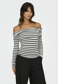 Langærmet off-shoulder top med sort og hvid vandret strib, lavet af blødt stof, parret med høj-taljede sorte bukser.