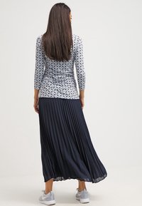 Lång marinblå veckad kjol i kombination med en figursydd grå mönstrad topp med trekvartslånga ärmar. Outfiten fulländas med grå sneakers.