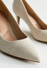 Tacchi alti beige con tomaia in tessuto testurizzato, punta affusolata e tacco sottile. La soletta è di un rosa chiaro, creando un contrasto con il materiale esterno.
